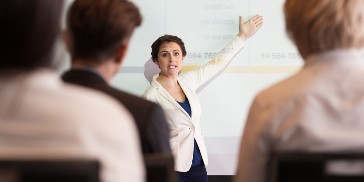 A trainer presenting medical coding information on a projected screen to a group of trainees during a classroom session.